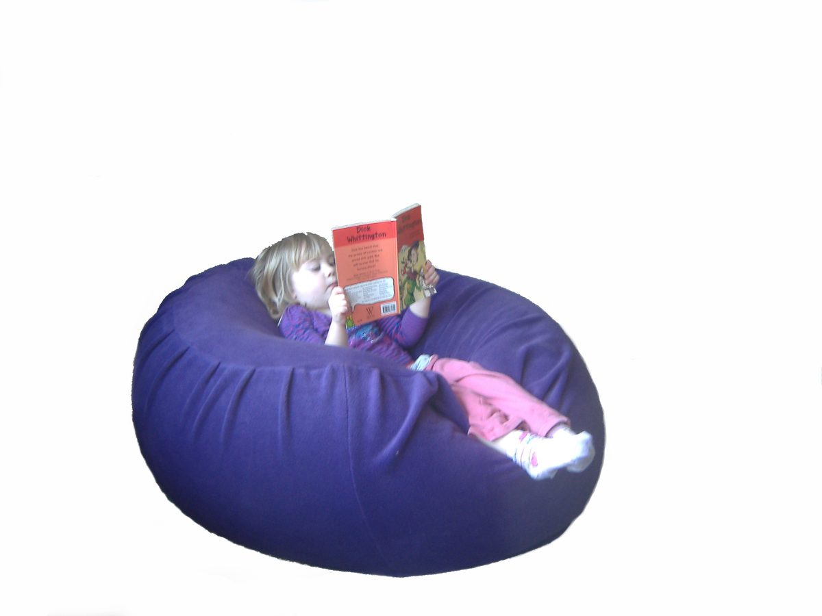 A young girl settled deep into a large purple fleece sensory beanbag, reading a book