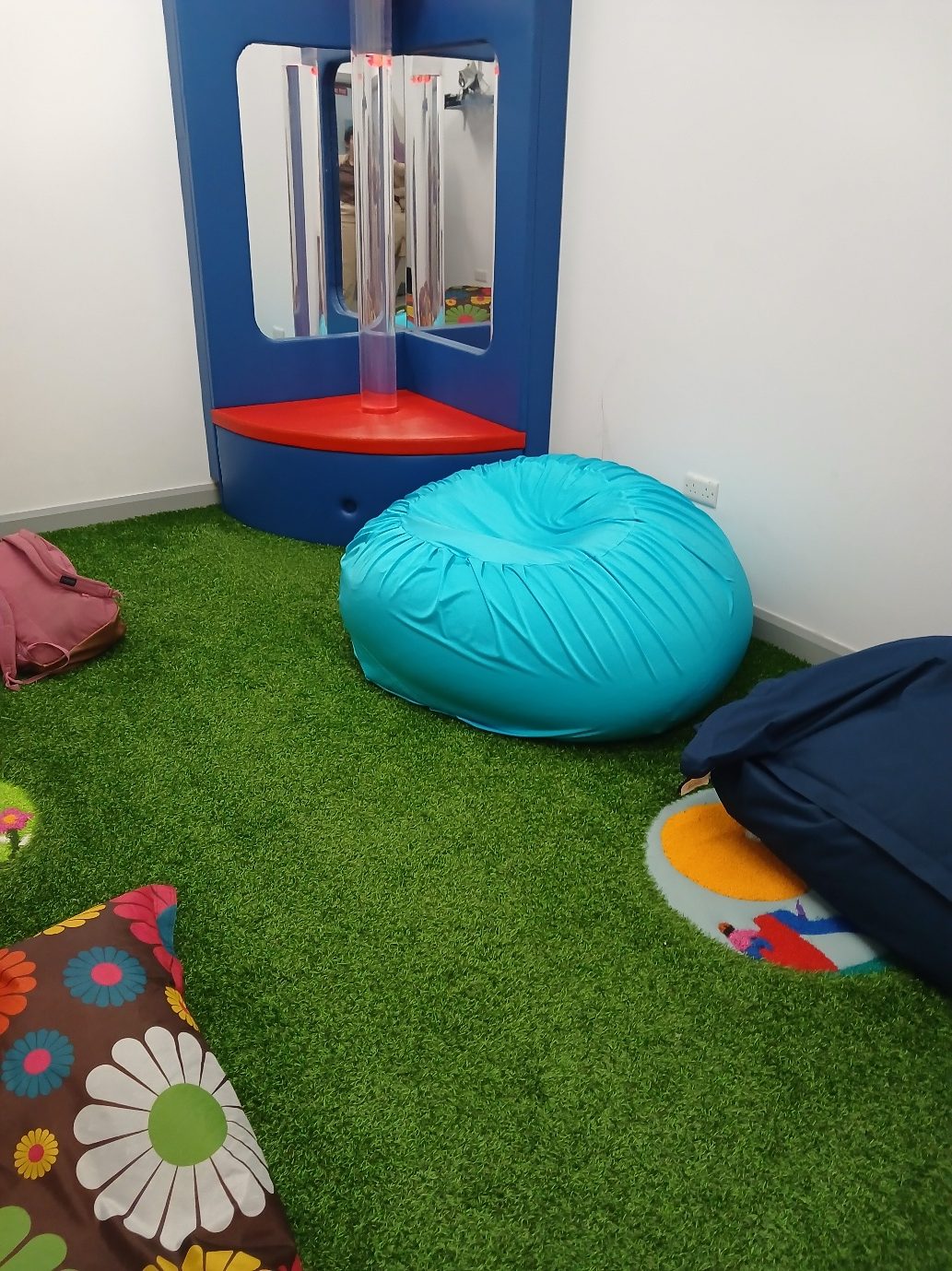 A turquoise stretch-lycra sensory beanbag on artificial grass in a sensory room, beside a mirror