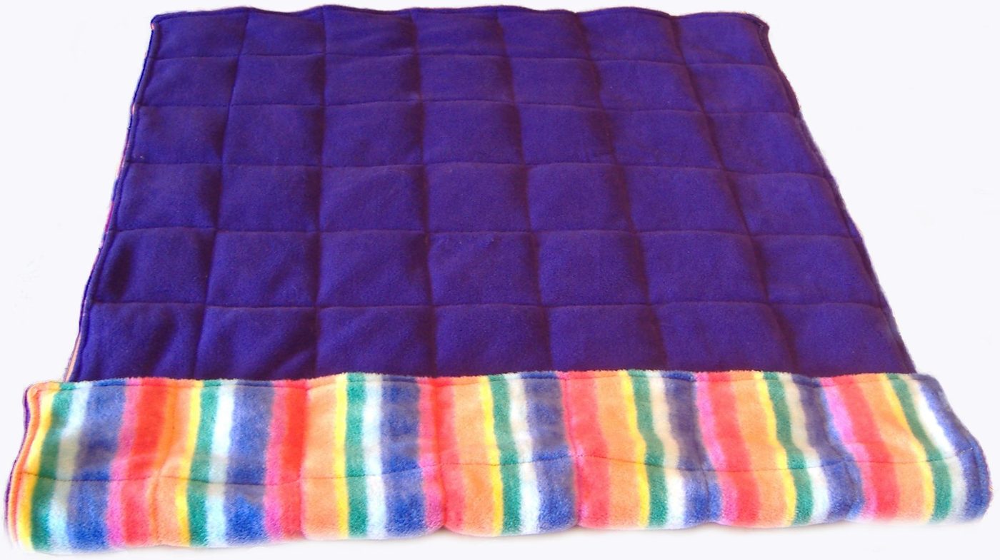 A purple weighted blanket, quilted into squares, folded back to show a rainbow-striped reverse